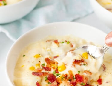 Hand holding a spoon scooping a bowl of Corn Chowder with Bacon.