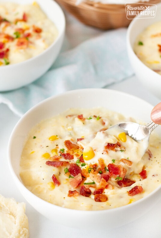 Hand holding a spoon scooping a bowl of Corn Chowder with Bacon.