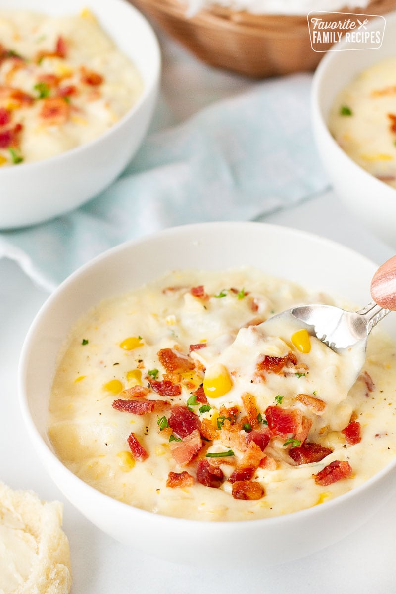 Hand holding a spoon scooping a bowl of Corn Chowder with Bacon.