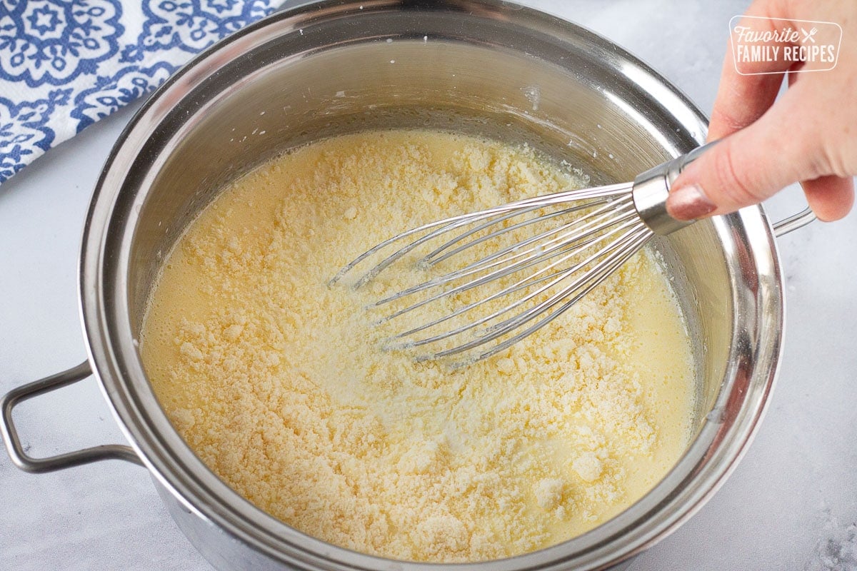 Whisk mixing a pot of Cream Sauce with parmesan cheese for Baked Cod.