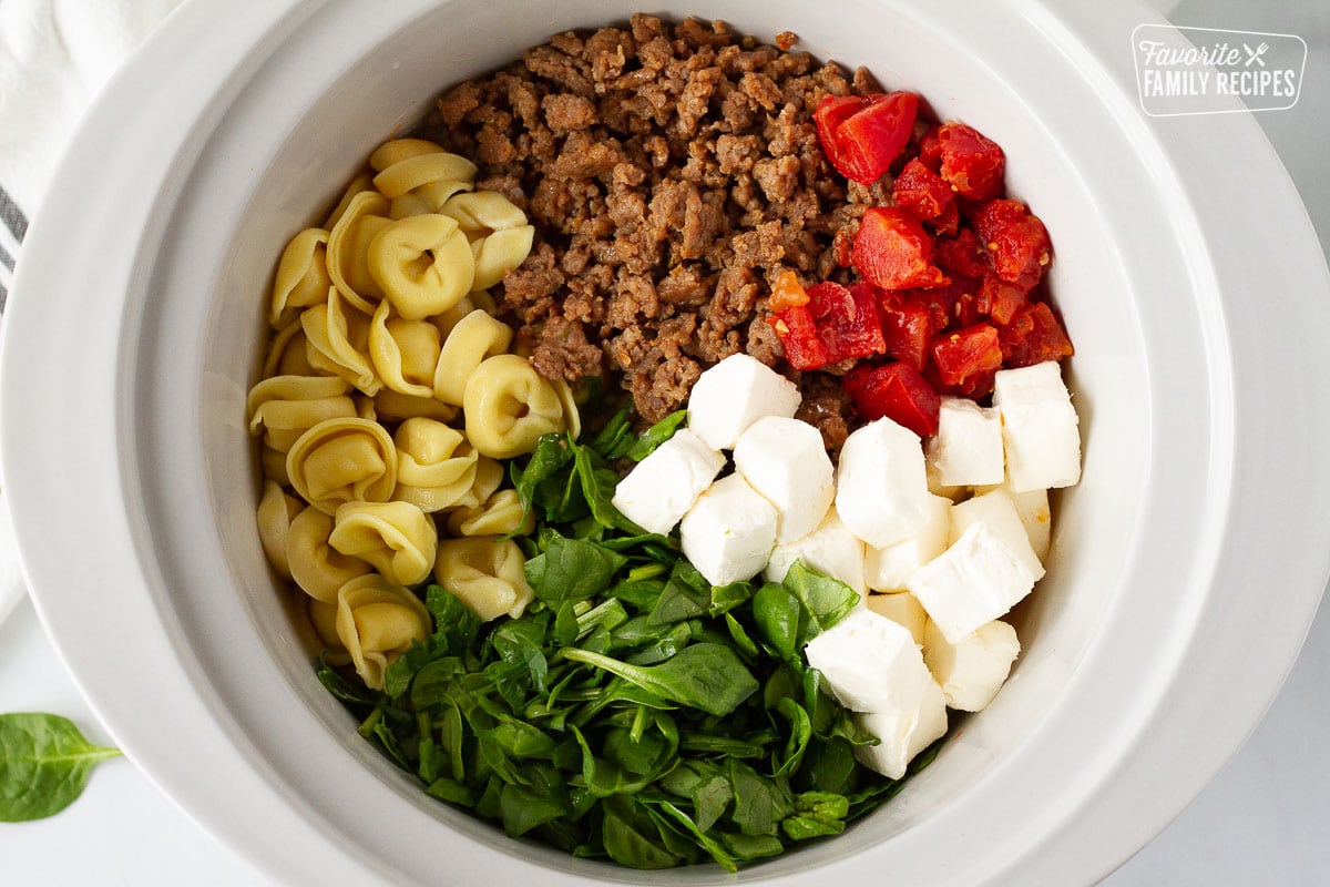 Slow cooker with spinach, tomatoes, Italian sausage, cheese tortellini and cream cheese for Creamy Tortellini Soup.