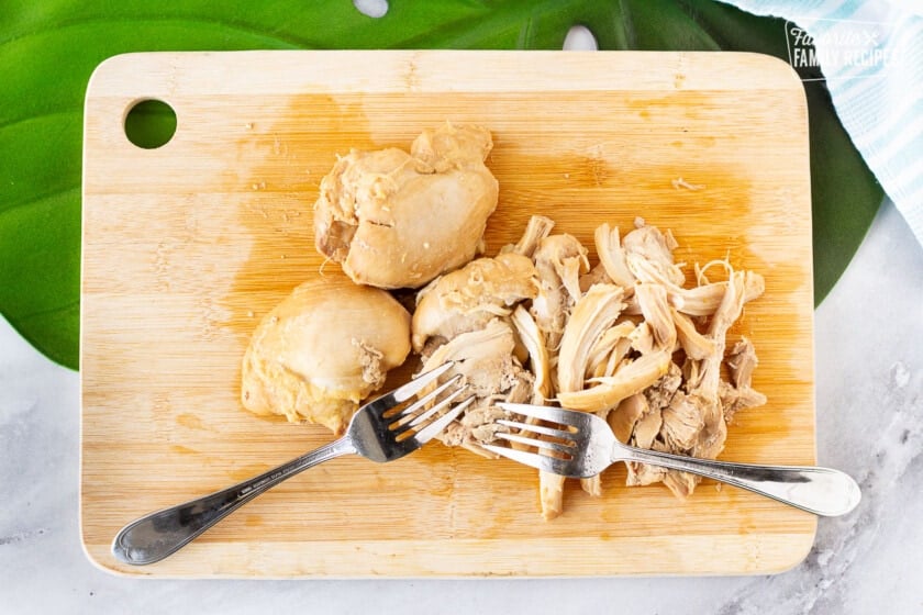 Cutting board with two forks shredding chicken thighs for Hawaiian Style Chicken Long Rice Noodles.