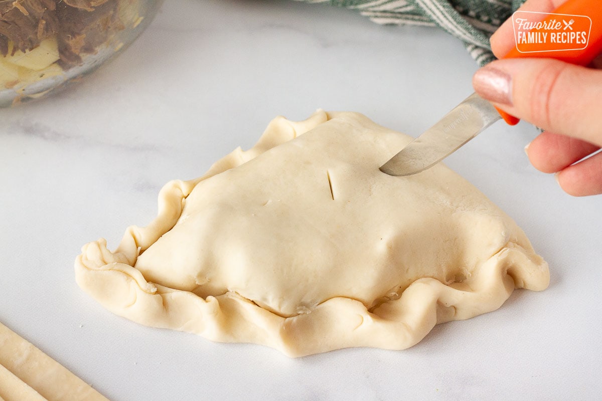 Hand holding a small knife cutting slits in the top of a single unbaked Donovan's Irish Pastie.