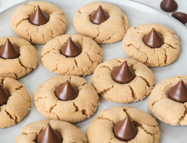 Peanut butter blossoms on a plate next to a glass jug of milk