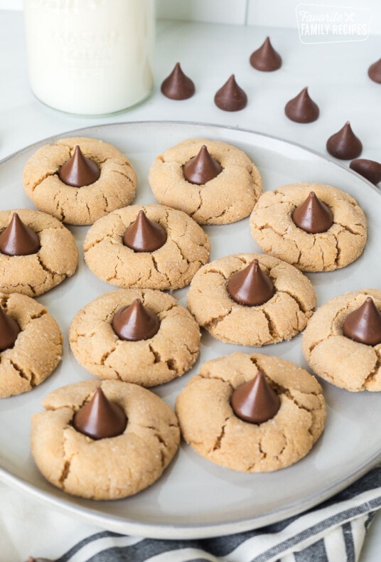 Peanut butter blossoms on a plate next to a glass jug of milk