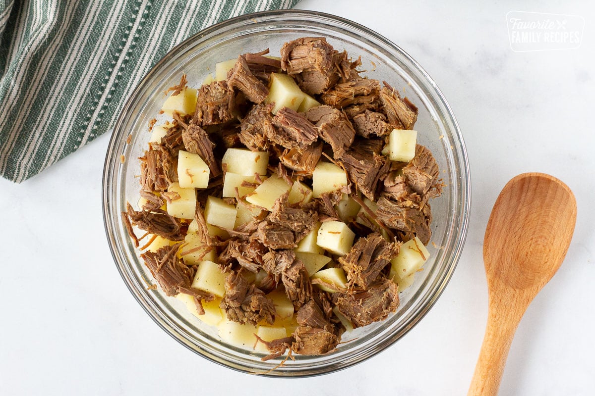 Beef and raw potato cubes mixed together in a bowl next to a wooden spoon for Donovan's Irish Pasties filling.