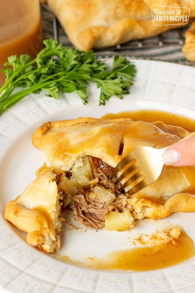 Hand holding a fork cutting into a Donovan's Irish Pastie with gravy.