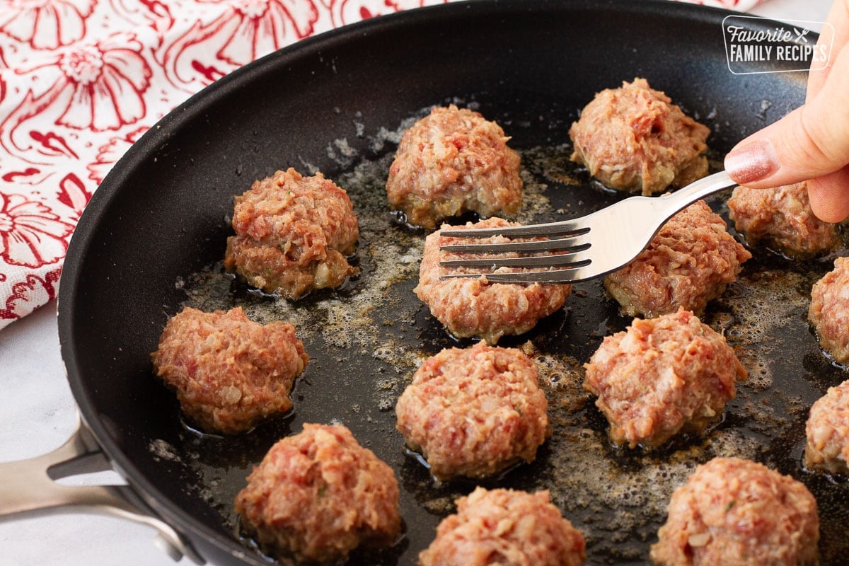 Fork pressing on Frikadeller (Danish Meatballs) in a skillet.