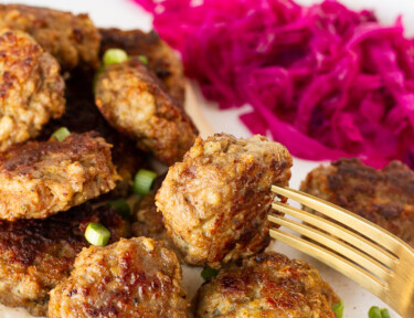 Fork resting on a plate with Frikadeller (Danish Meatballs) and red cabbage.