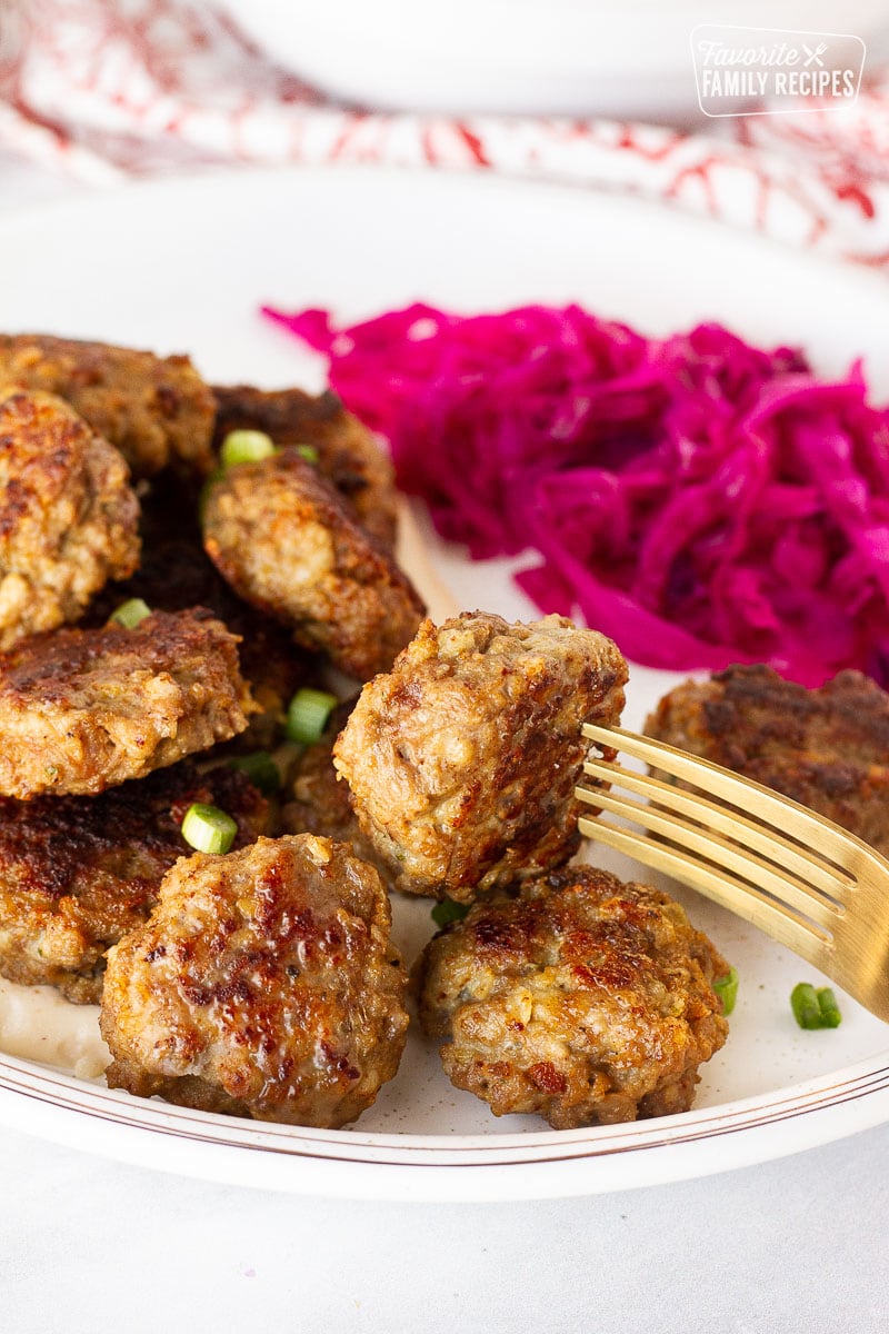 Fork resting on a plate with Frikadeller (Danish Meatballs) and red cabbage.