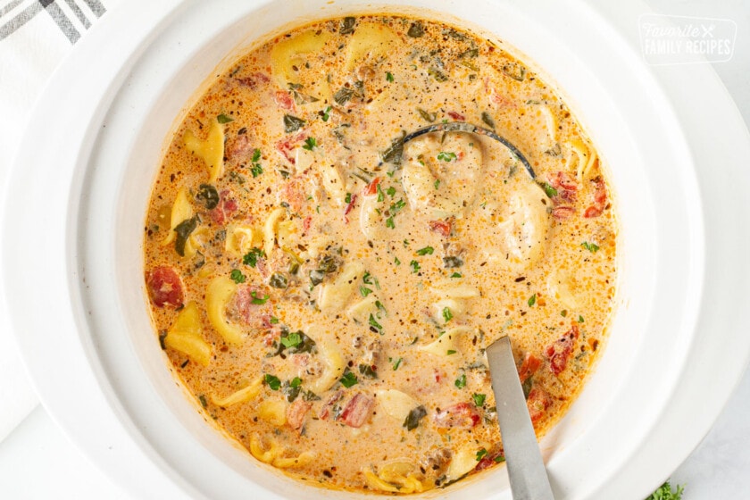 Slow cooker full of Creamy Tortellini Soup and ladle.
