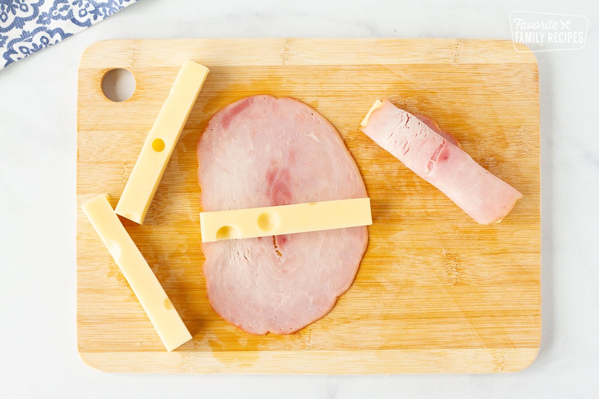 Cutting board with ham and Swiss cheese for Chicken Cordon Bleu.