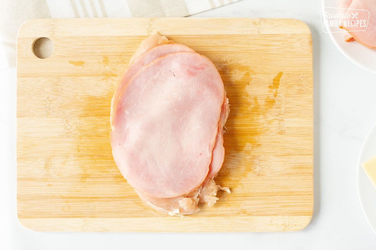 Flattened chicken breast on a cutting board covered with two slices of Black Forest ham for Instant Pot Chicken Cordon Bleu.