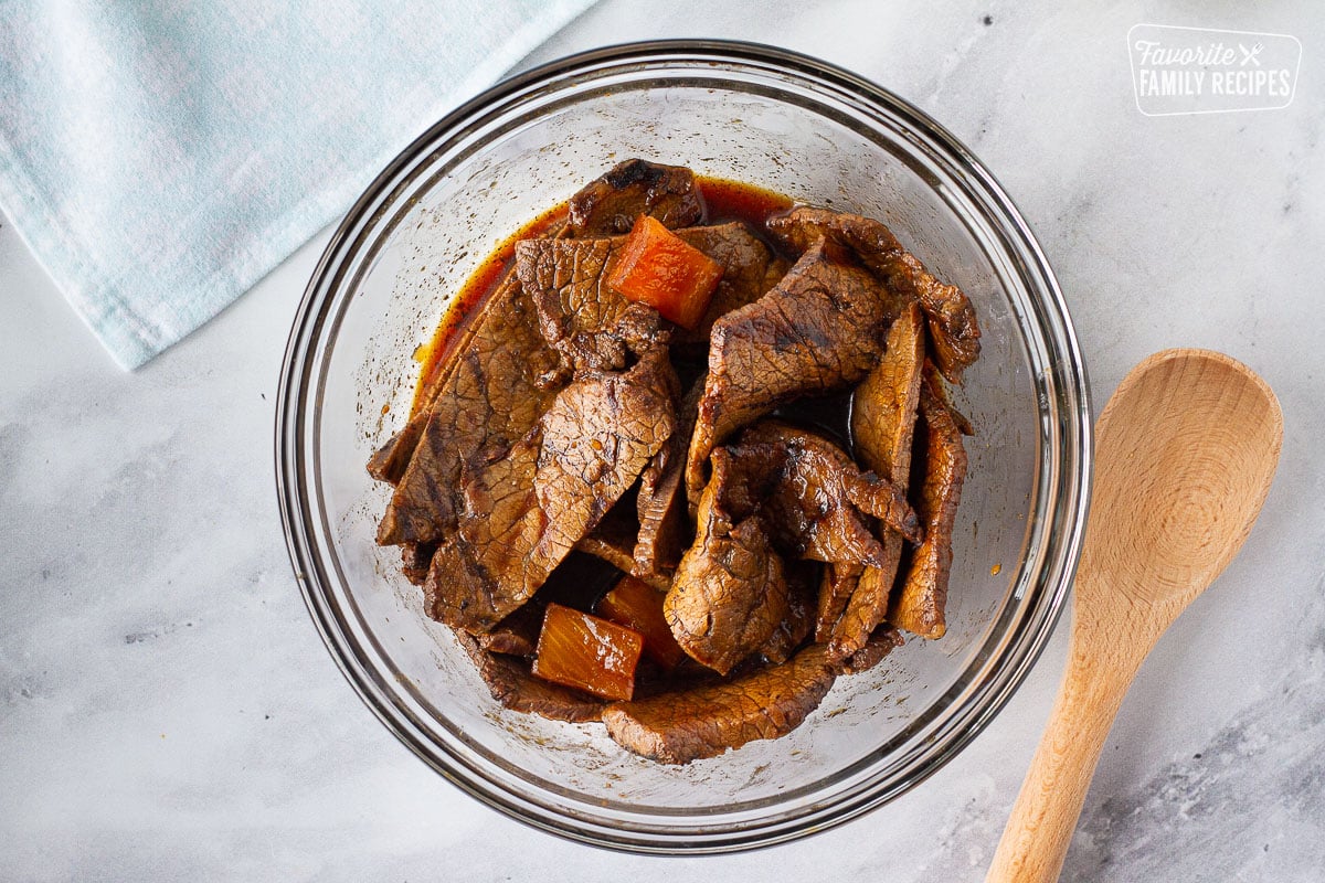 Sliced grilled Teriyaki Beef in a glass bowl with extra marinade.