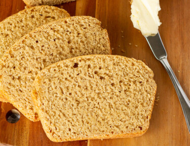 Three slices of Honey Whole Wheat Bread on a c cutting board next to a butter knife.