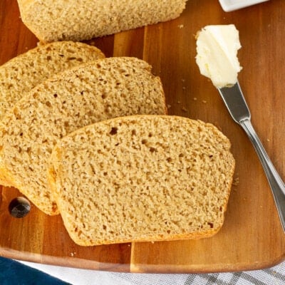 Three slices of Honey Whole Wheat Bread on a c cutting board next to a butter knife.