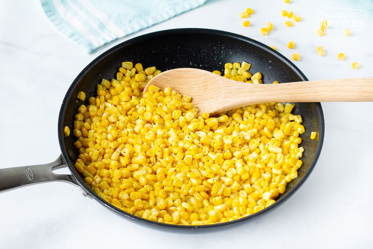 Skillet of Cooked Frozen Corn with a wooden spoon.