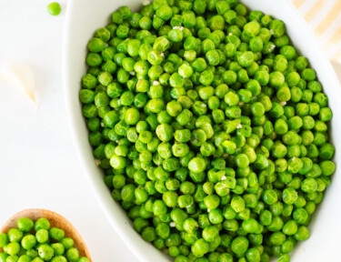 Top view of How to Cook Frozen Peas next to a wooden spoon full of Cooked Peas.