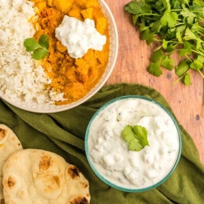 A bowl of raita next to a bowl of chicken tikka masala and rice.