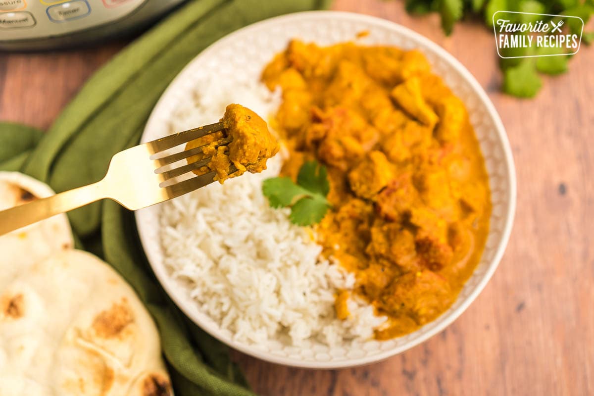 A bowl of rice and chicken tikka masala with a forkful of chicken