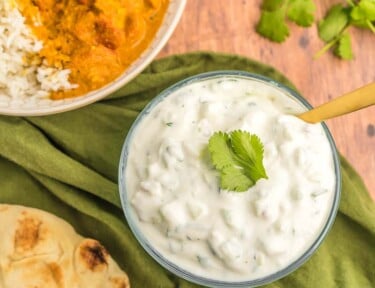 A bowl of raita next to a bowl of chicken tikka masala and rice