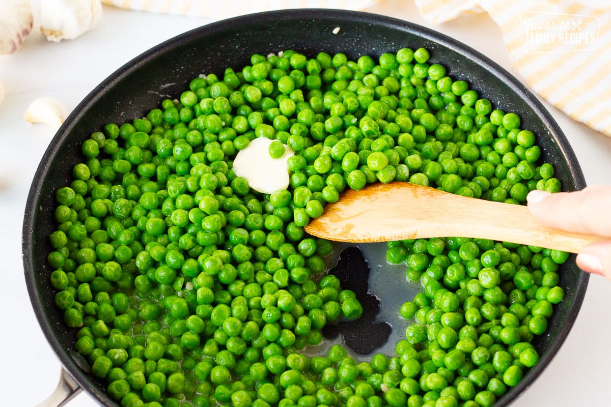 Wooden spoon stirring and cooking Frozen Peas.