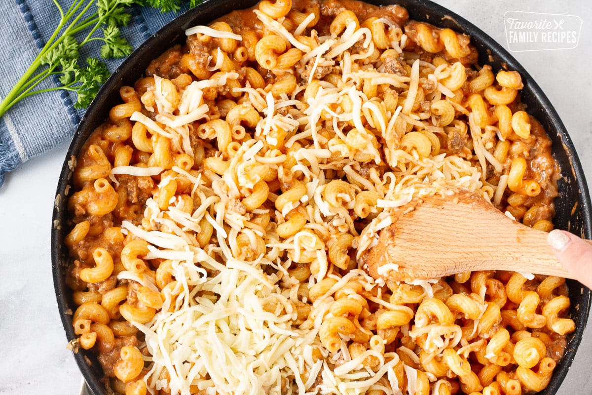 Stirring in cheese with a wooden spoon for Creamy Ground Beef and Noodles Skillet.