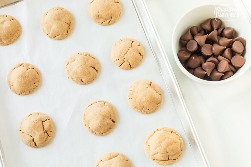 Peanut butter cookies on a cookie sheet next to a bowl of unwrapped Hershey's kisses