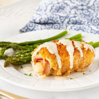 Single Chicken Cordon Bleu next to asparagus on a plate.