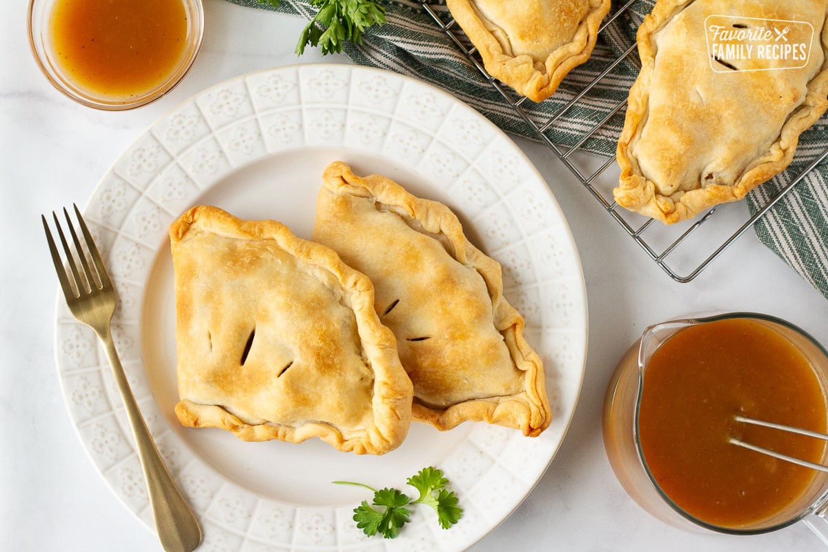 Plate with two baked Irish Pasties. Gravy and extra pasties on the side.