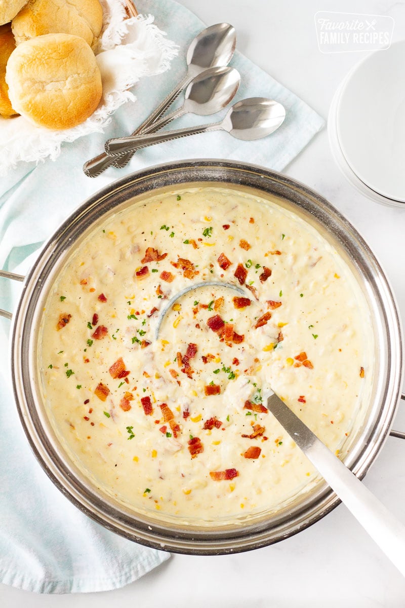 Soup pot of Corn Chowder with Bacon. Rolls, bowls and spoons on the side.