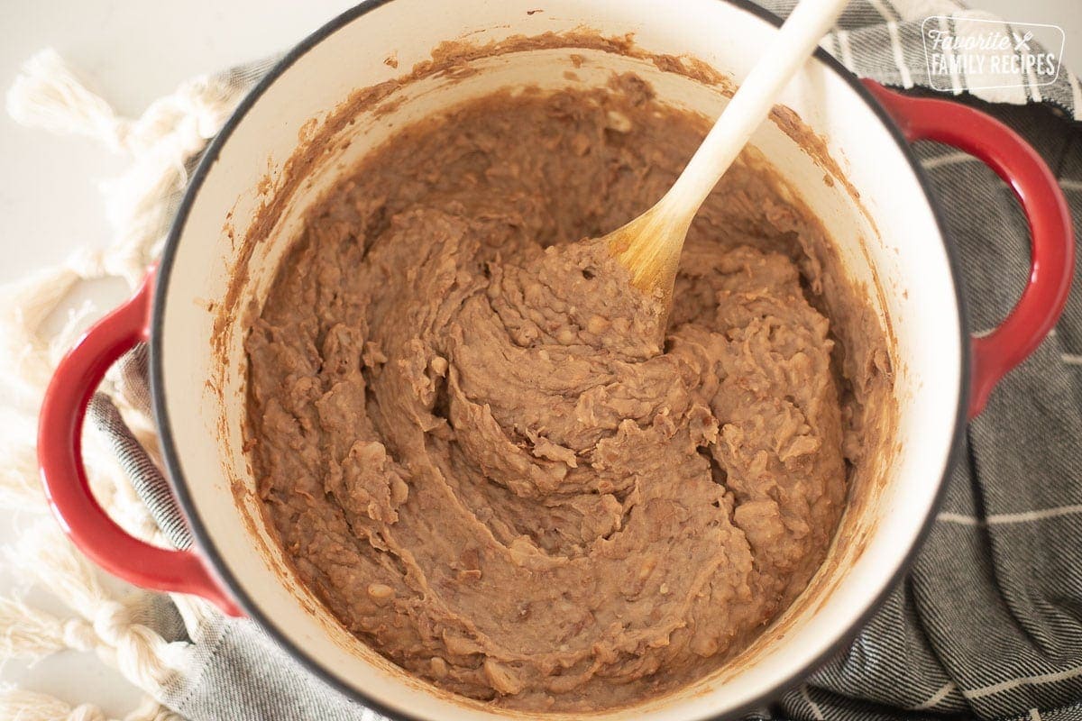 A ceramic Dutch oven with homemade refried beans being stirred.
