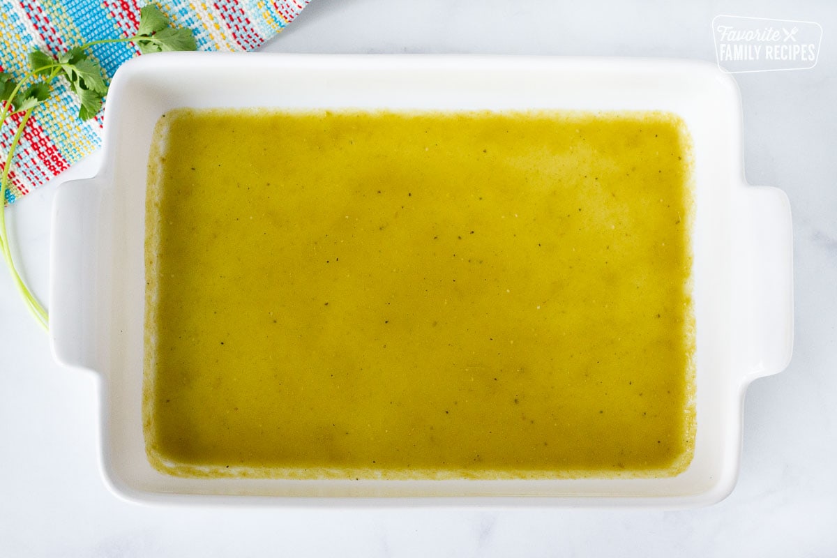 Baking dish with green enchilada sauce layered on the bottom.