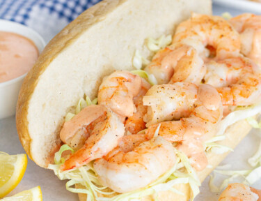 Shrimp Po'Boy Sandwich with shredded cabbage and sauce. Lemon wedges on the side.