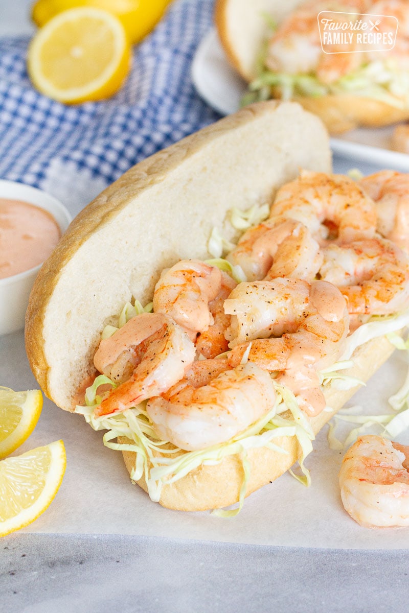 Shrimp Po'Boy Sandwich with shredded cabbage and sauce. Lemon wedges on the side.