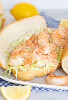 Three Shrimp Po'Boy Sandwiches on a plate with a dish of extra cajun sauce and lemon slices on the side.