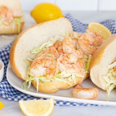Three Shrimp Po'Boy Sandwiches on a plate with a dish of extra cajun sauce and lemon slices on the side.