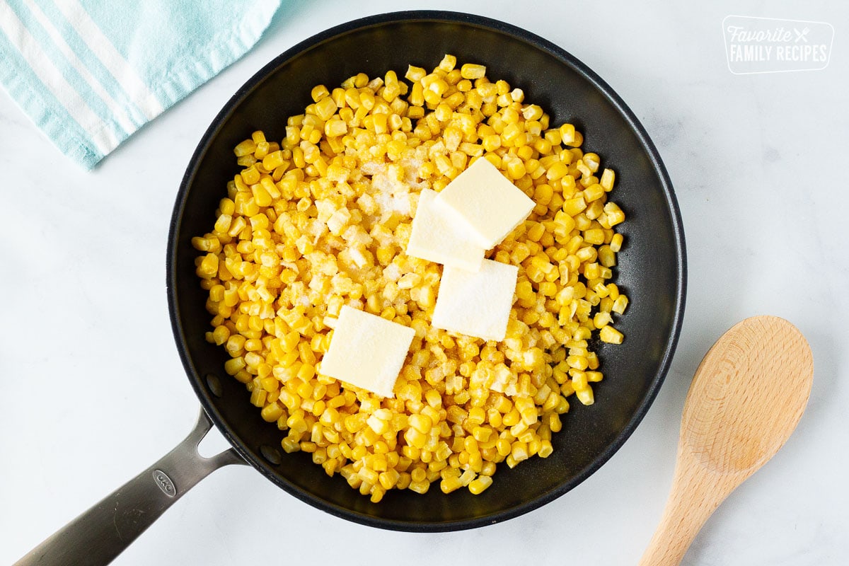 Frozen corn in a skillet with butter and sugar to cook.