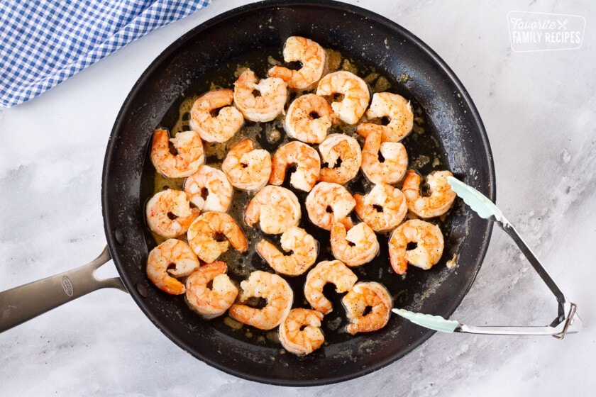 Cooked shrimp in a skillet for Shrimp Po'Boy Sandwiches with tongs.
