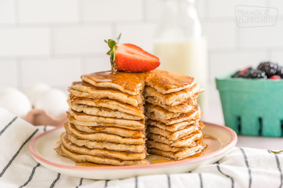 A stack of sourdough pancakes with a slice cut out topped with syrup and a strawberry