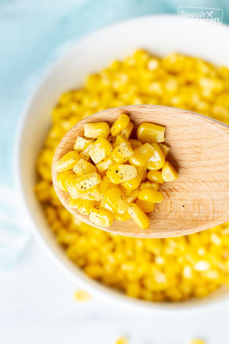Wooden spoon holding cooked frozen corn with pepper.