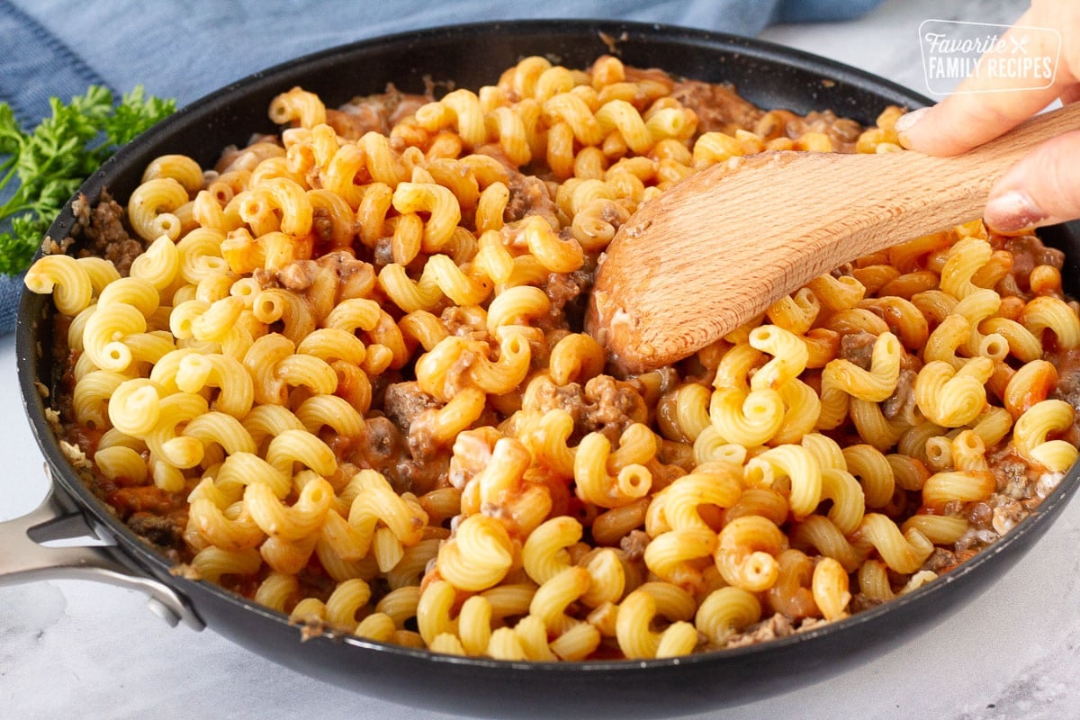 Mixing noodles into the ground beef sauce with a wooden spoon for Creamy Ground Beef and Noodles Skillet.