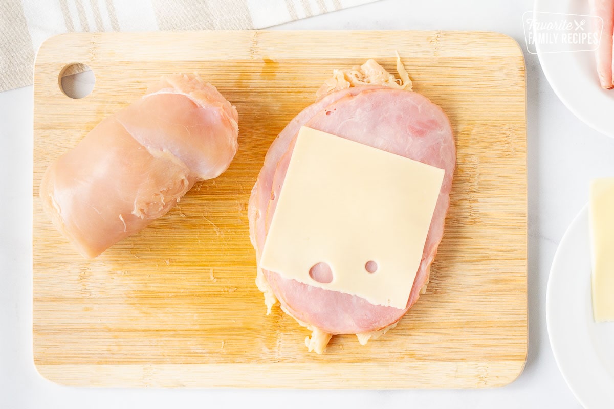 Cutting board with one rolled up chicken breast and one chicken breast topped with Black Forest ham and Swiss cheese for Instant Pot Chicken Cordon Bleu.