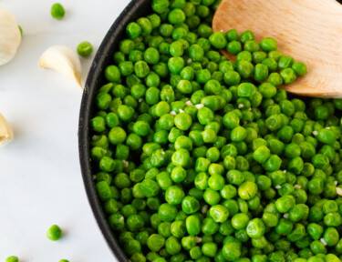 Skillet with Cooked Frozen Peas and a wooden spoon.