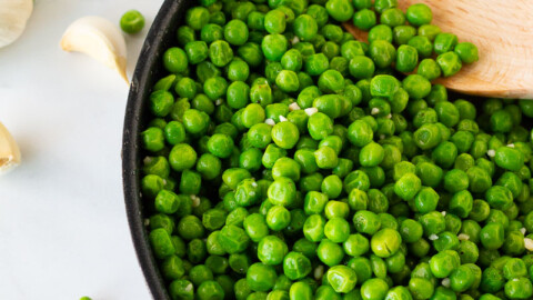 Skillet with Cooked Frozen Peas and a wooden spoon.