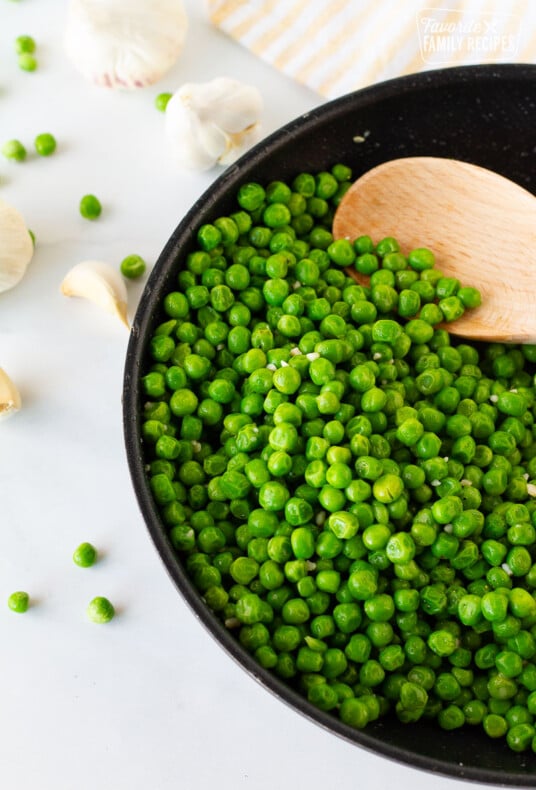 Skillet with Cooked Frozen Peas and a wooden spoon.