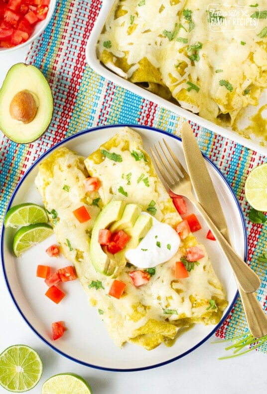 Plate of Spinach Enchiladas with avocados, cilantro, sour cream and tomatoes.