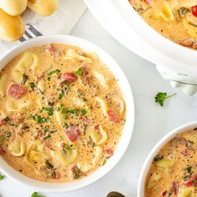 Crockpot of Creamy Tortellini Soup next to two bowls of Creamy Tortellini Soup and breadsticks.
