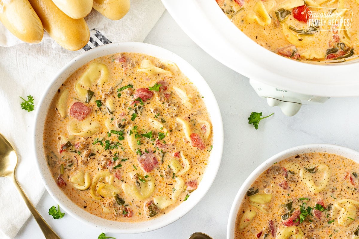 Crockpot of Creamy Tortellini Soup next to two bowls of Creamy Tortellini Soup and breadsticks.