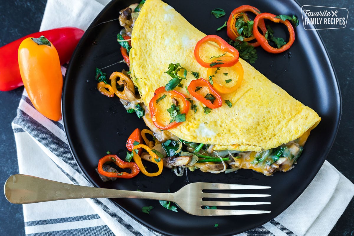 A veggie omelette on a plate with sautéed mushrooms, spinach, and peppers